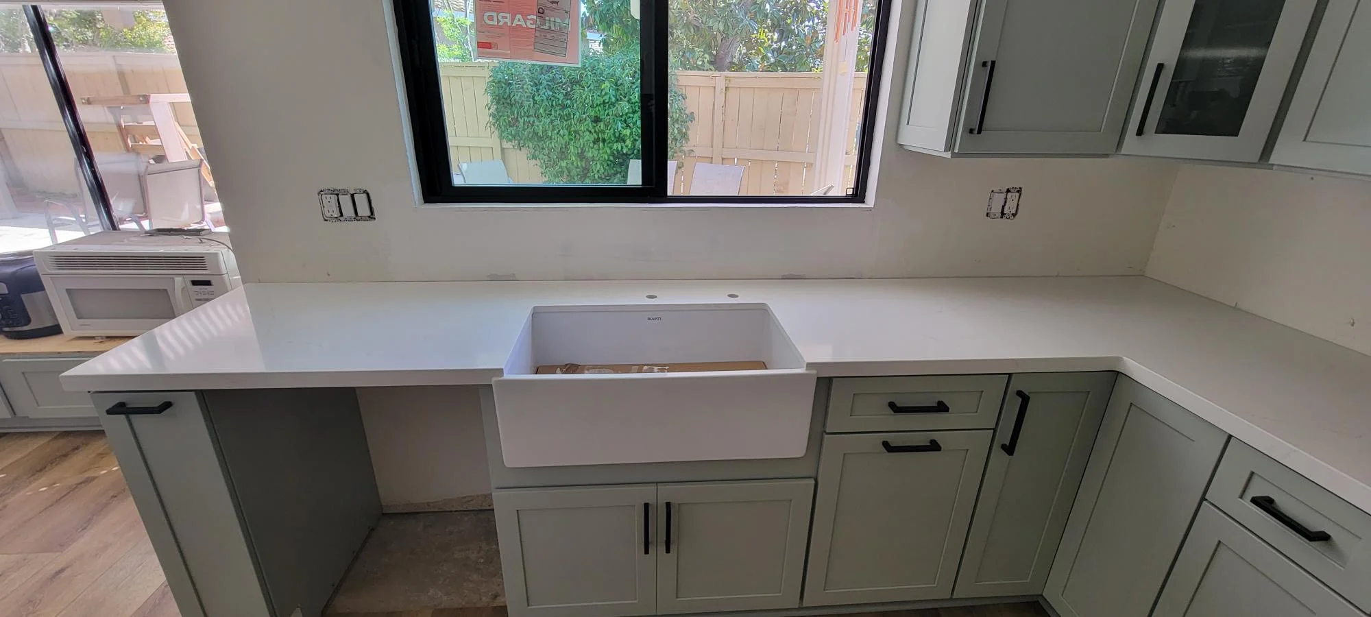 Kitchen with sage green cabinets, white quartz counters, and white farmhouse sink under black-framed window