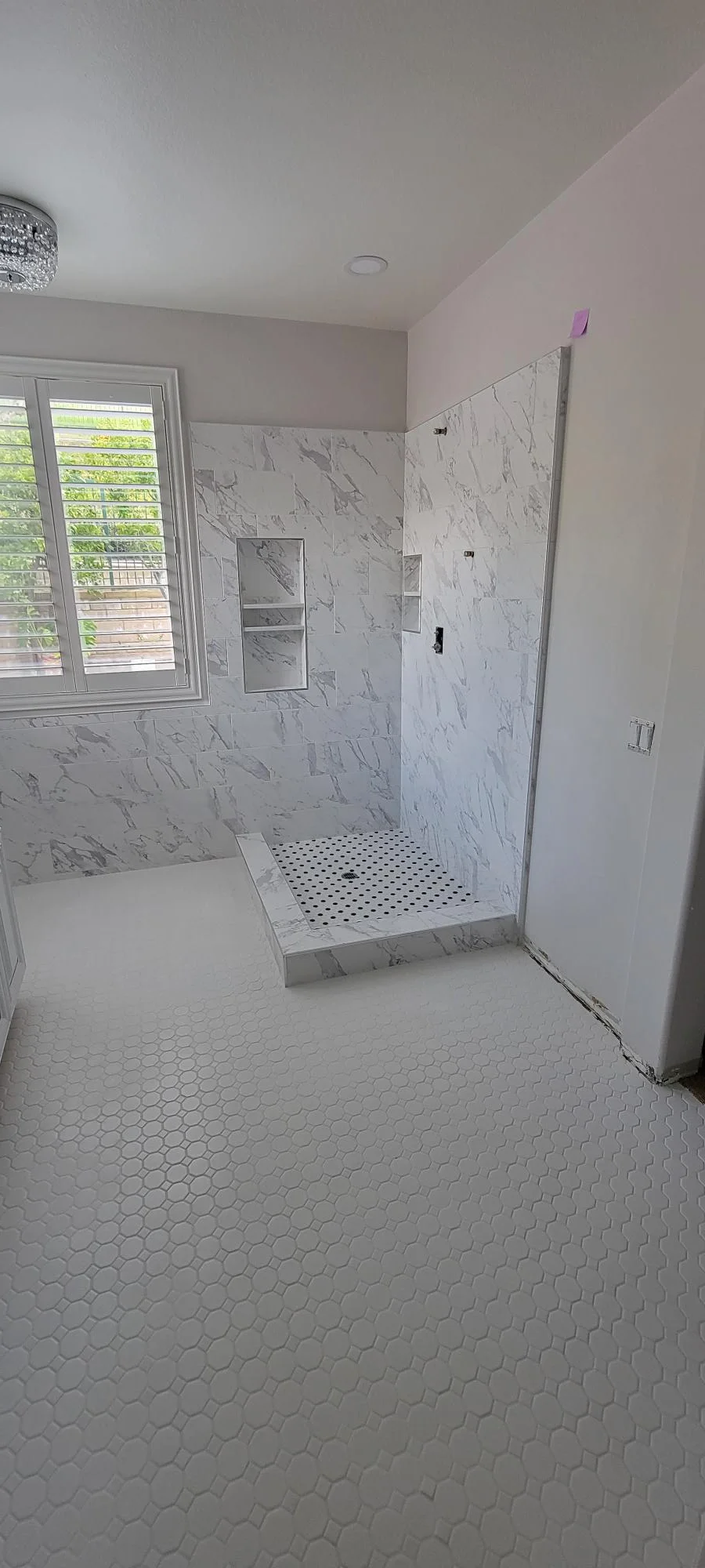 Marble tile shower with frameless glass door and hexagonal floor tile in renovated bathroom