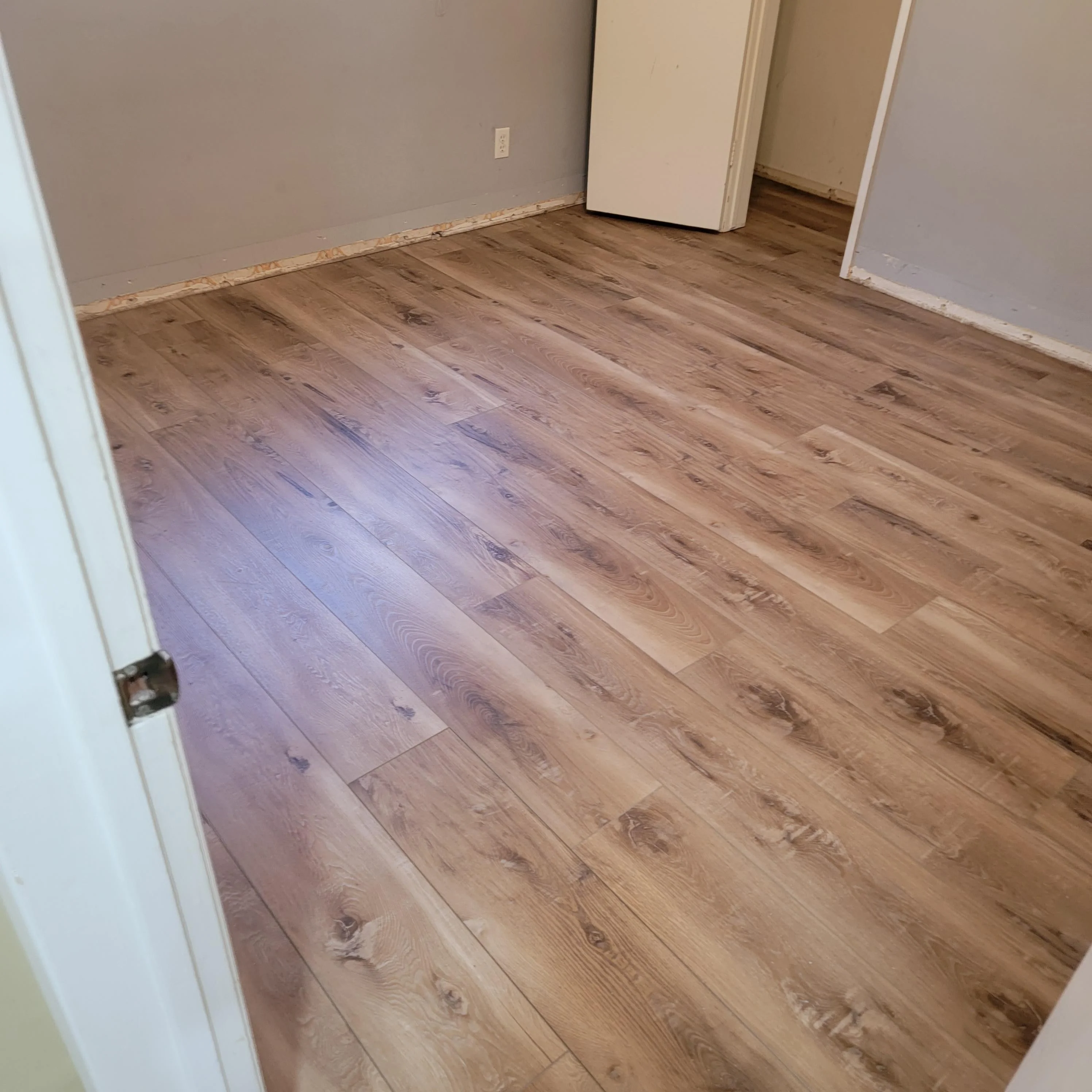 Luxury vinyl plank flooring with wood-grain pattern installed in bedroom with white trim