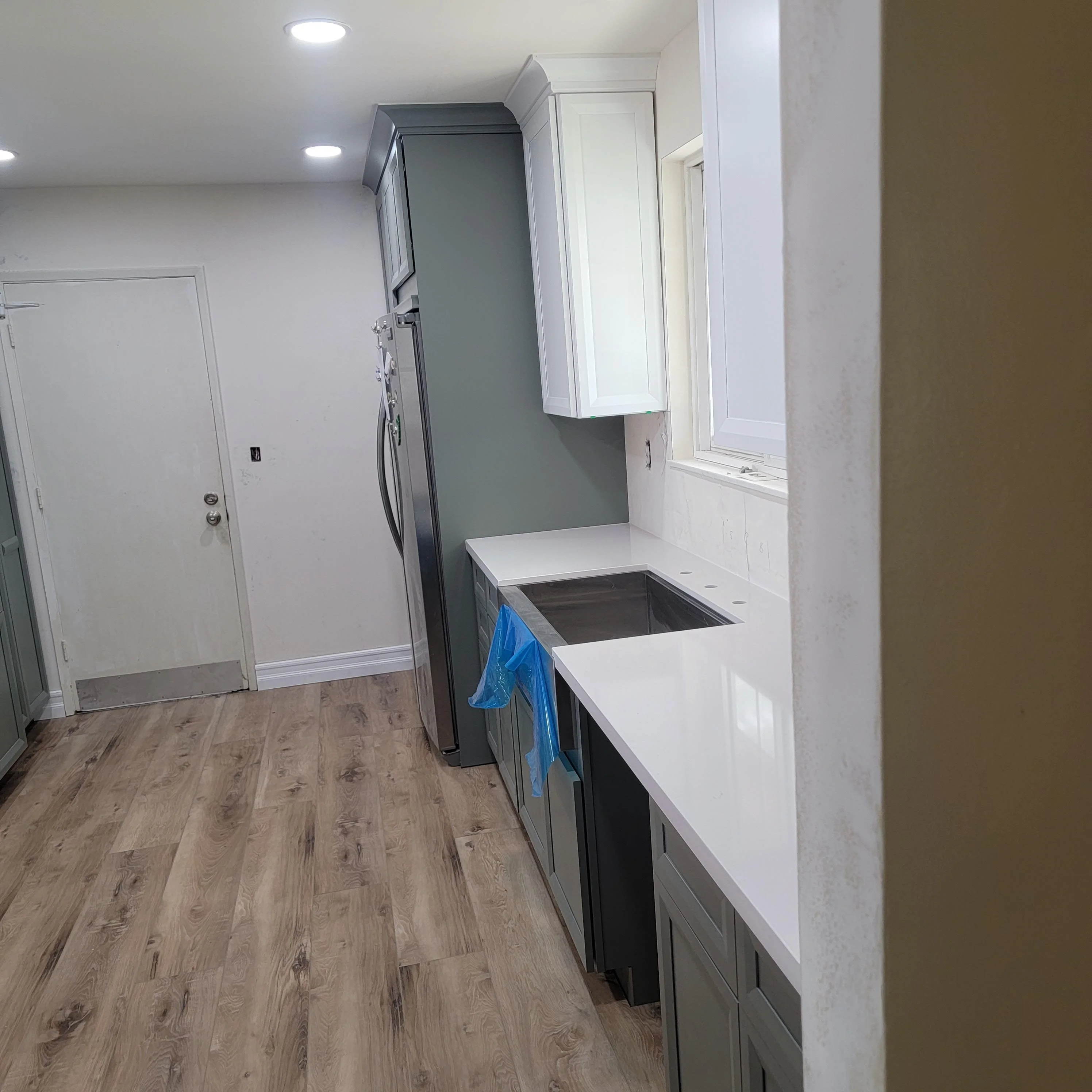 Kitchen with dark cabinetry, white quartz counters, stainless steel appliances, and vinyl plank flooring