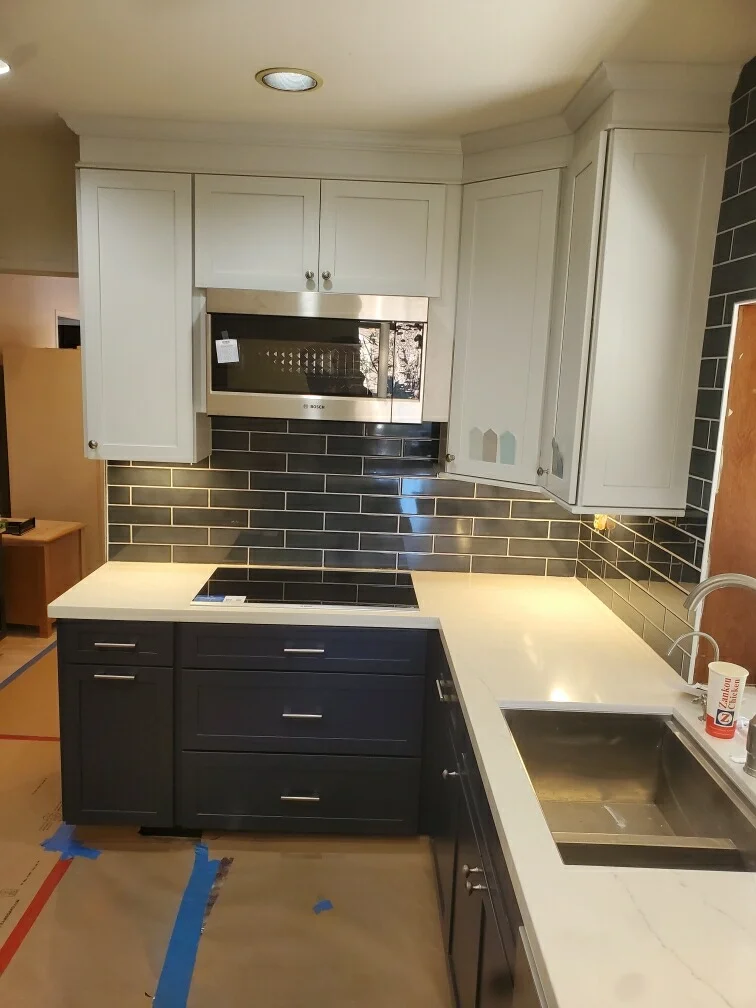 Kitchen with white upper cabinets, dark lower cabinets, white quartz counters, black subway tile backsplash, stainless steel appliances