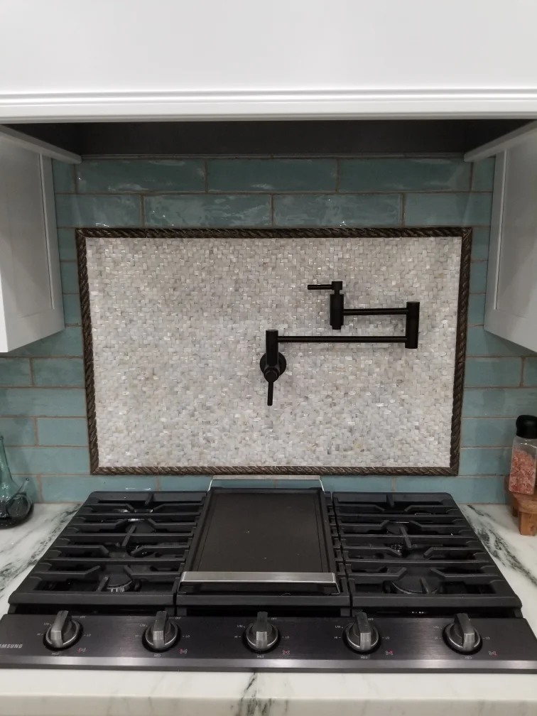 Light gray mosaic tile backsplash with rope trim above black gas cooktop and teal subway tile accents