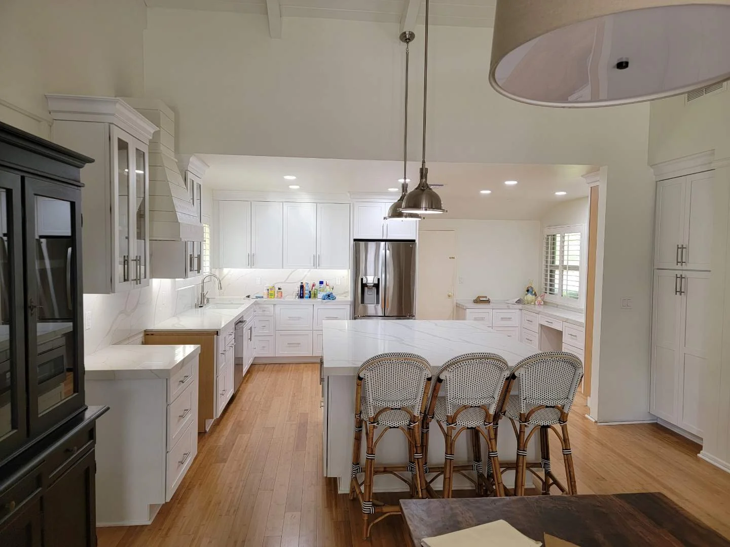 White kitchen with marble island, stainless appliances, hardwood floors, and pendant lighting