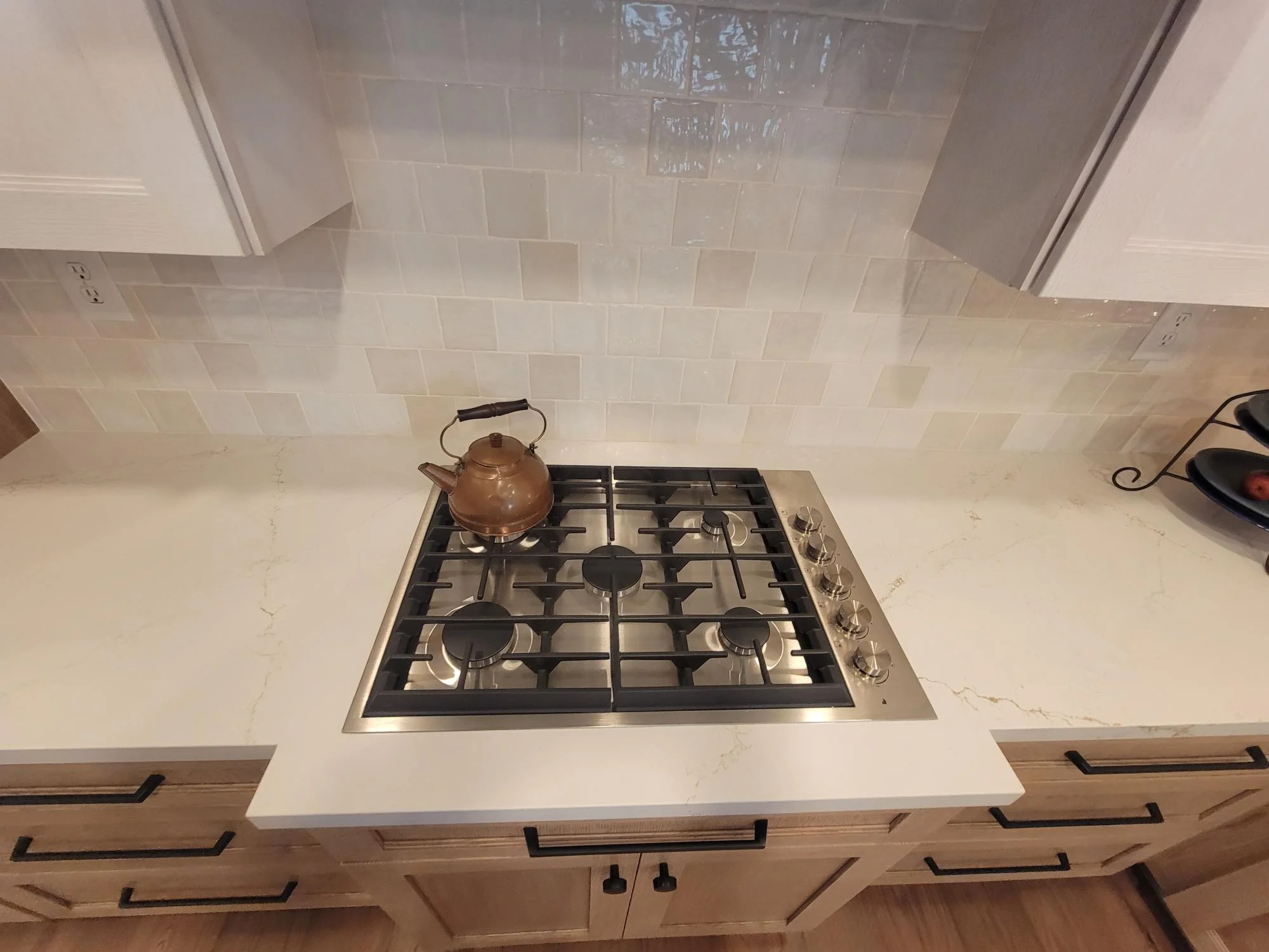 Gas cooktop with stainless steel frame on white quartz counter, cream subway tile backsplash, wood cabinetry