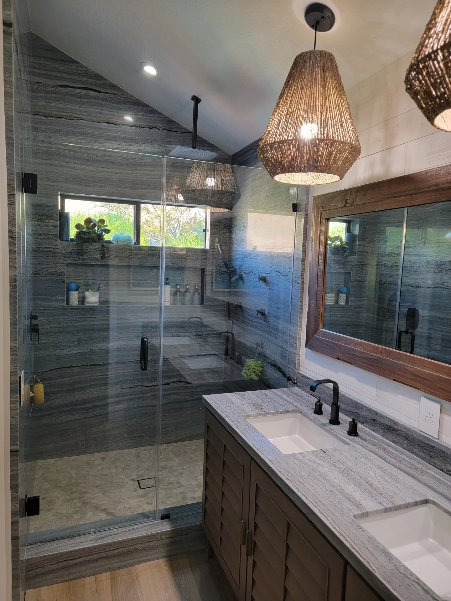 Master bathroom with gray tile shower, quartz vanity, frameless glass enclosure, and woven pendant lights