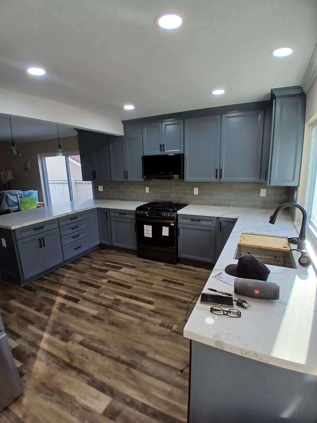 Gray kitchen cabinets, white quartz counters, subway tile backsplash, black range, vinyl plank flooring