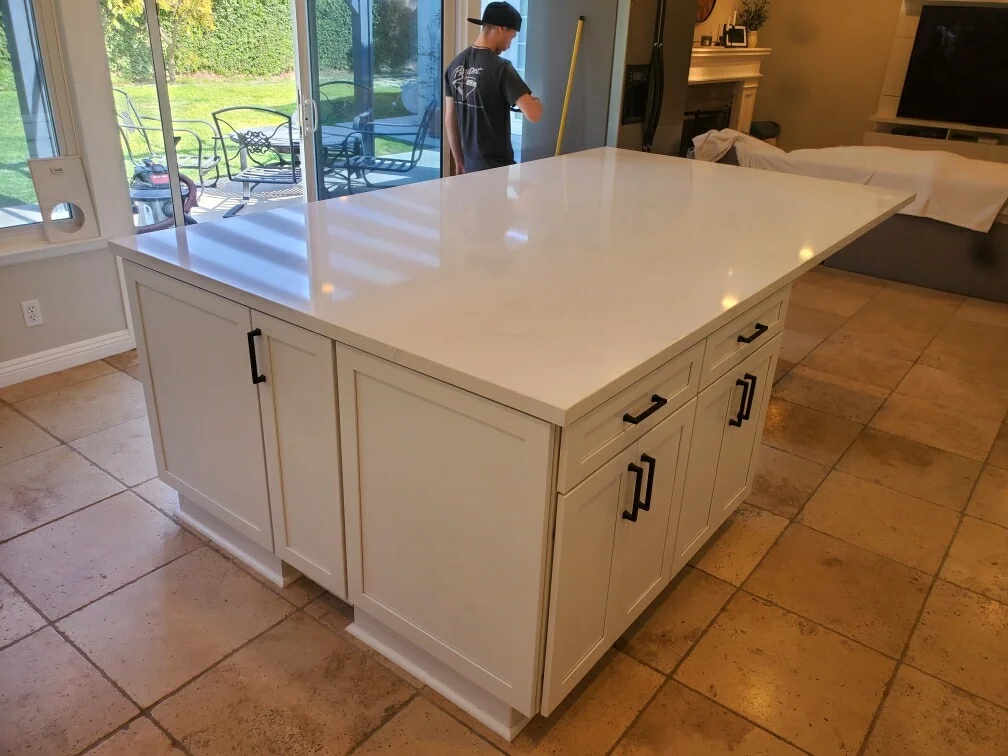 White kitchen island with quartz countertop and black hardware on tile floor