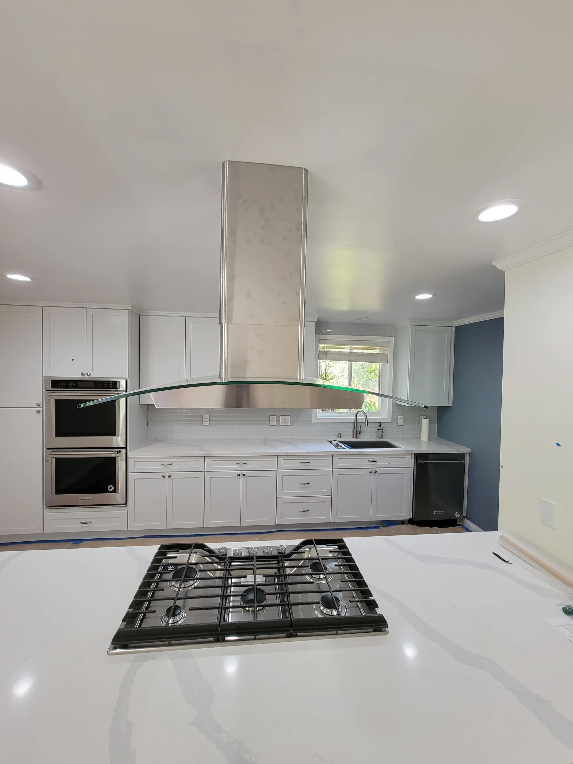 White kitchen cabinetry with stainless steel appliances, quartz countertops, and curved glass range hood