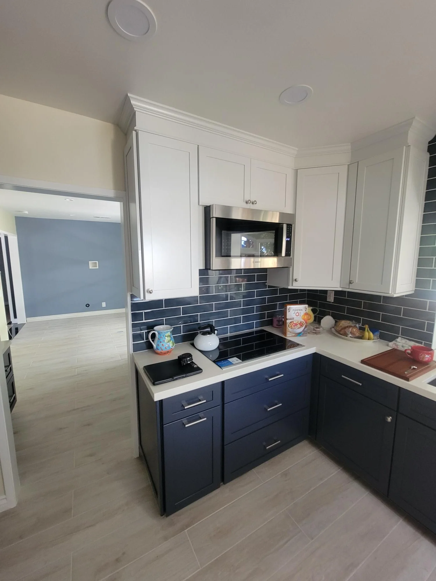 Kitchen with white upper cabinets, navy lower cabinets, dark subway tile backsplash, quartz counters, and stainless steel appliances