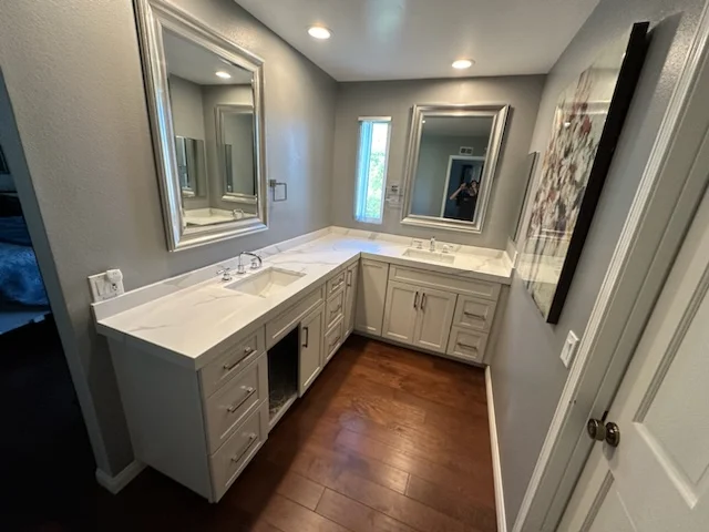 Master bathroom with double vanity, quartz counters, white cabinetry, and wood flooring