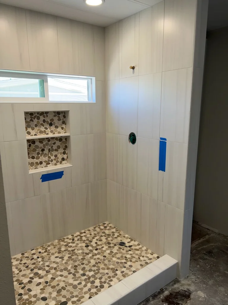 White subway tile shower with pebble mosaic niche and stone floor, recessed shelving, transom window