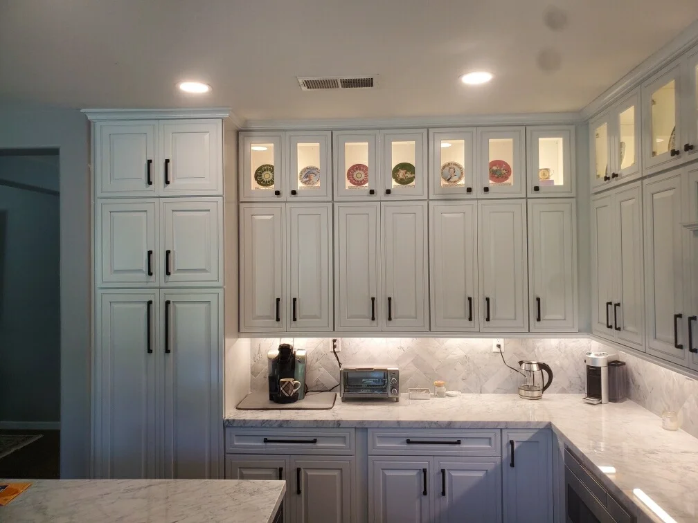 White shaker cabinets with marble countertops, glass-front uppers, and under-cabinet lighting
