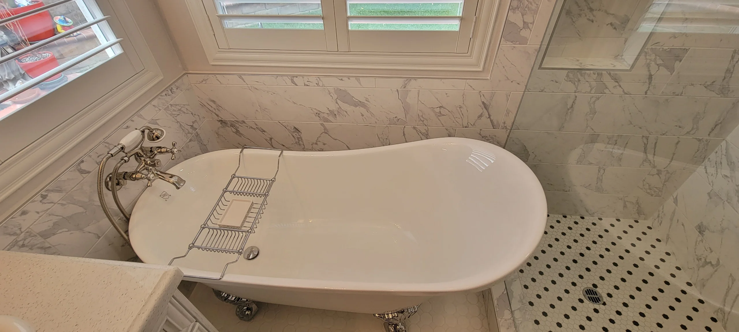 Freestanding soaking tub with marble tile walls and ceiling, chrome fixtures, and skylight in luxury bathroom