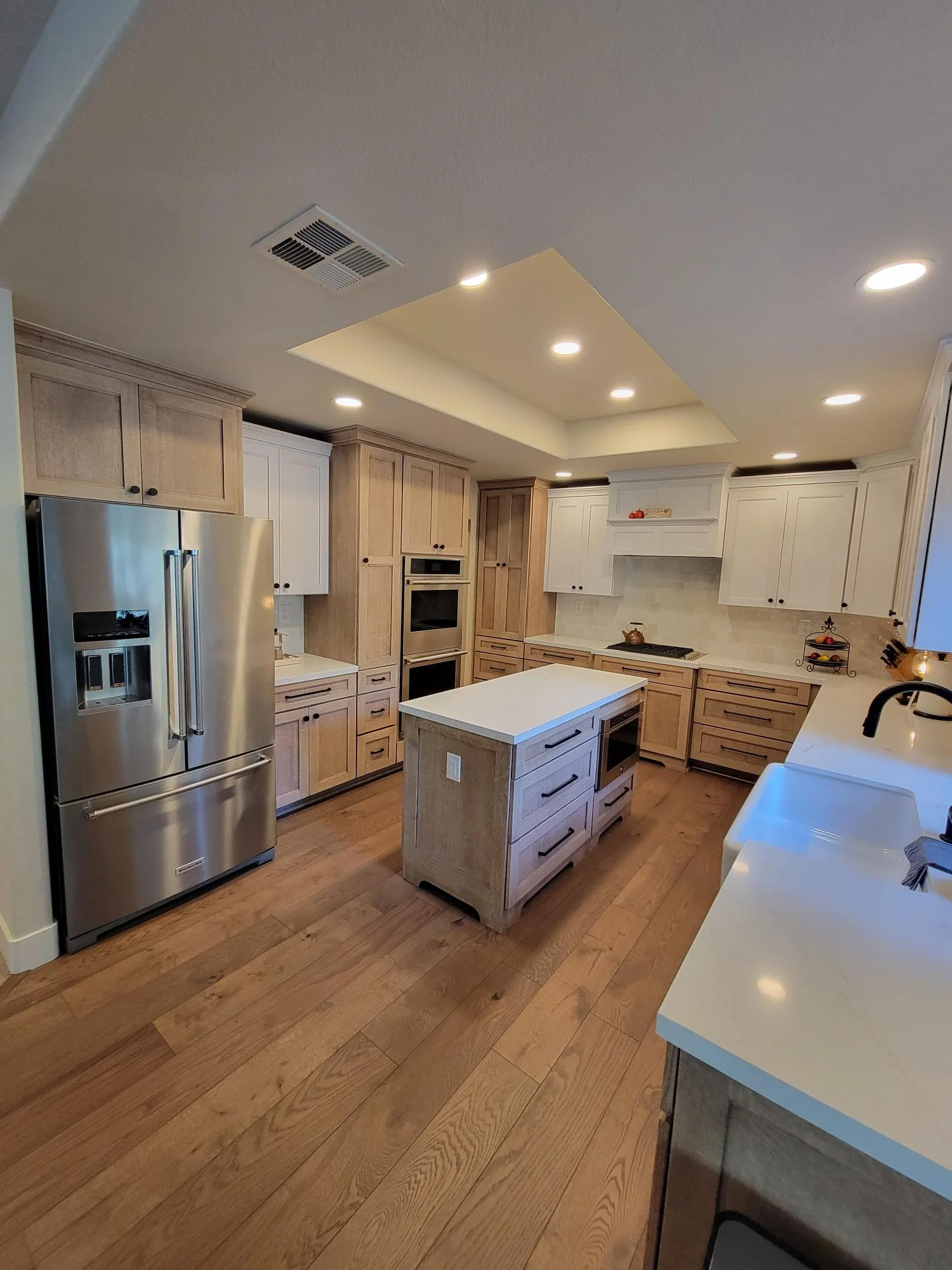 Kitchen with wood and white cabinetry, stainless steel appliances, hardwood floors, and coffered ceiling with recessed lights