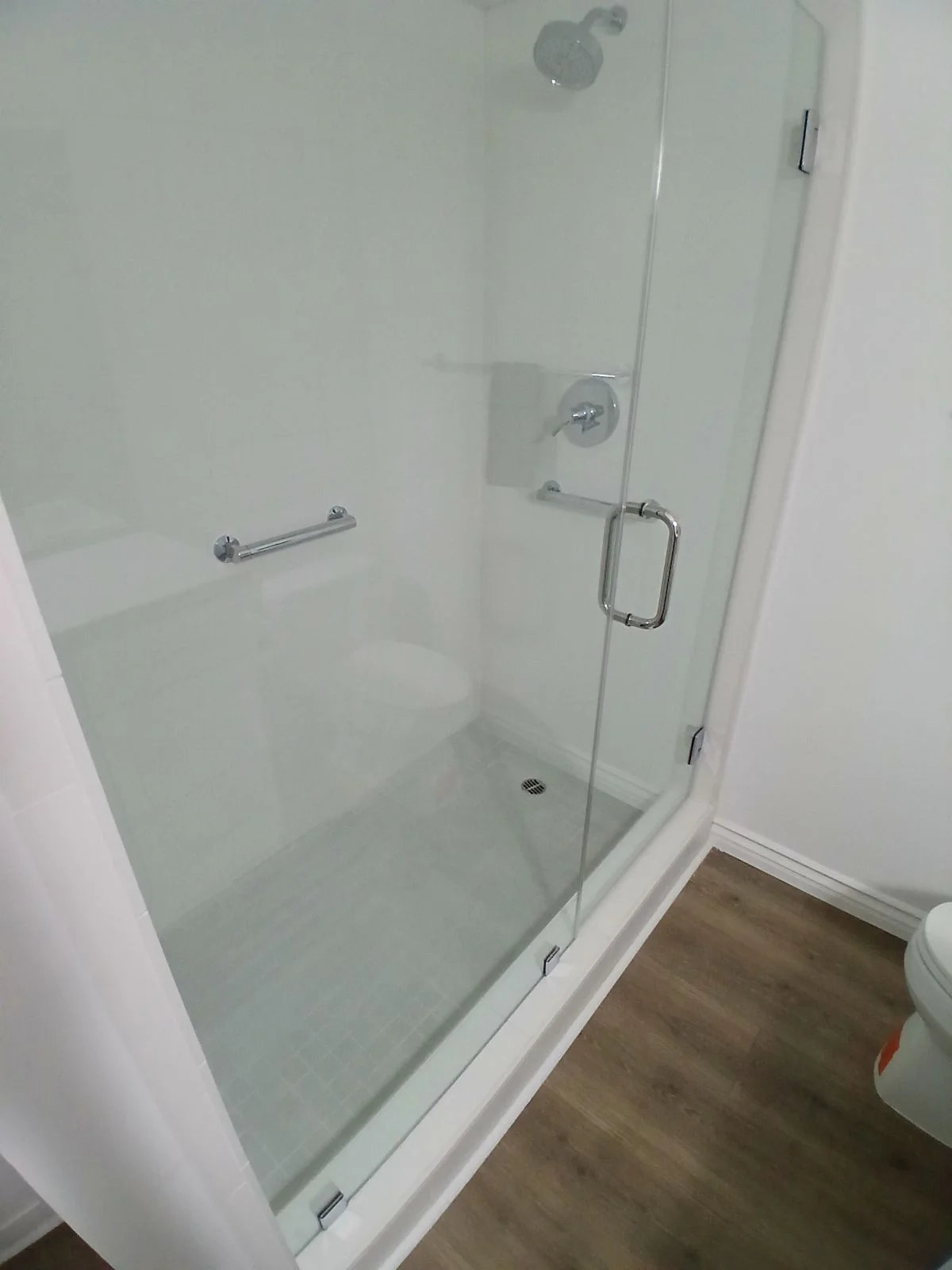 Frameless glass shower enclosure with chrome hardware and stainless steel grab bar