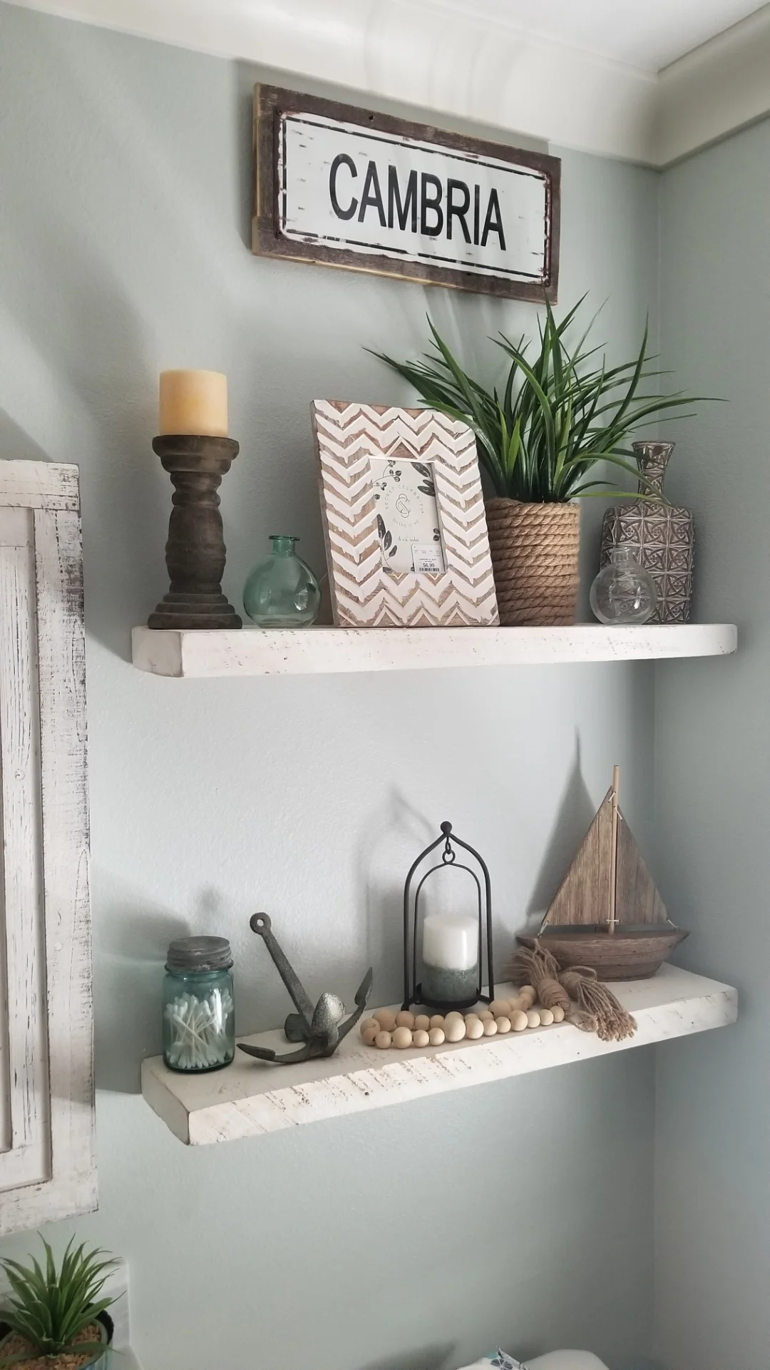 Two white floating shelves mounted on sage-green wall with decorative items and potted plants