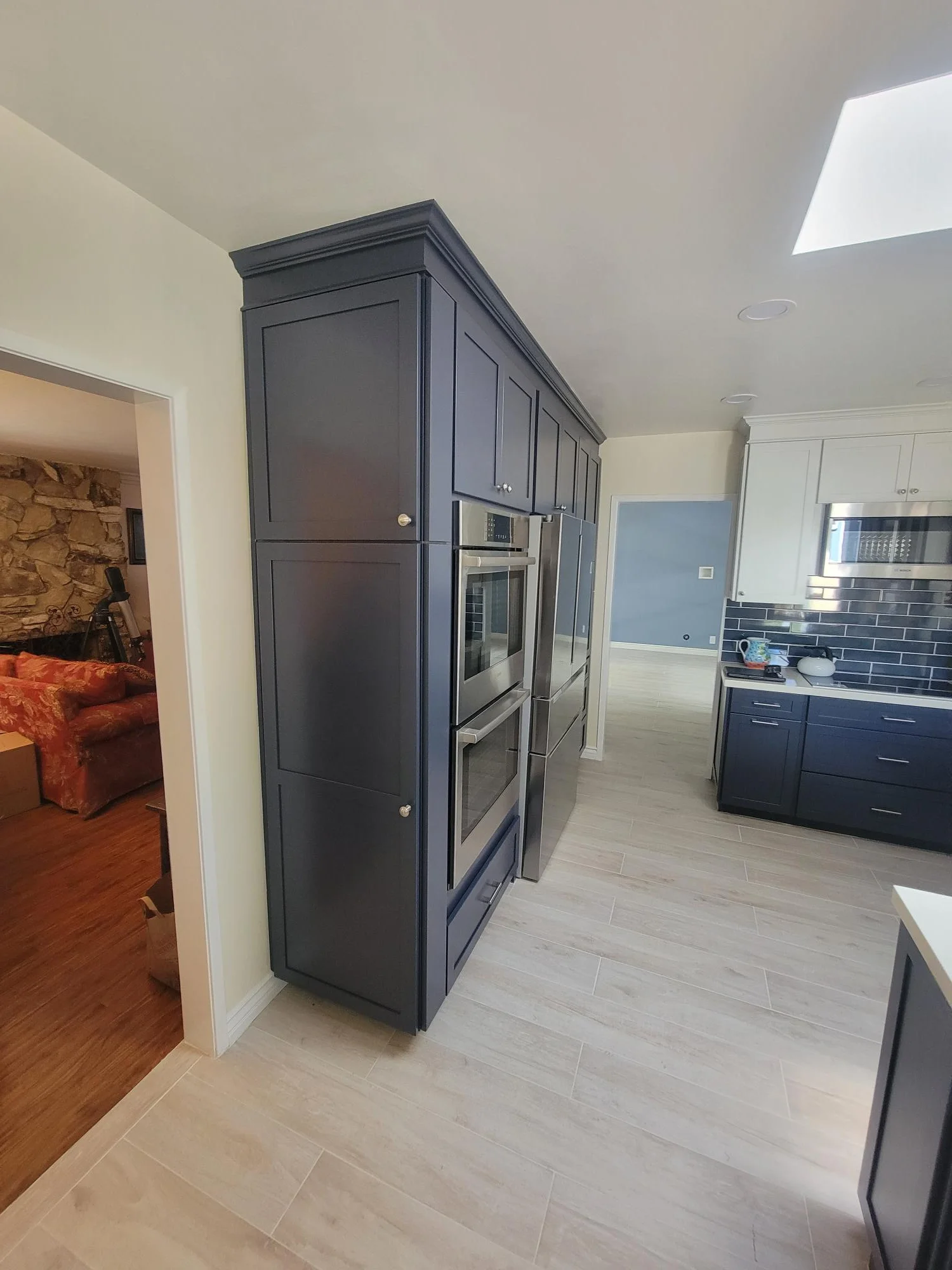 Custom dark gray kitchen cabinetry with integrated double ovens, light tile flooring, and white subway backsplash