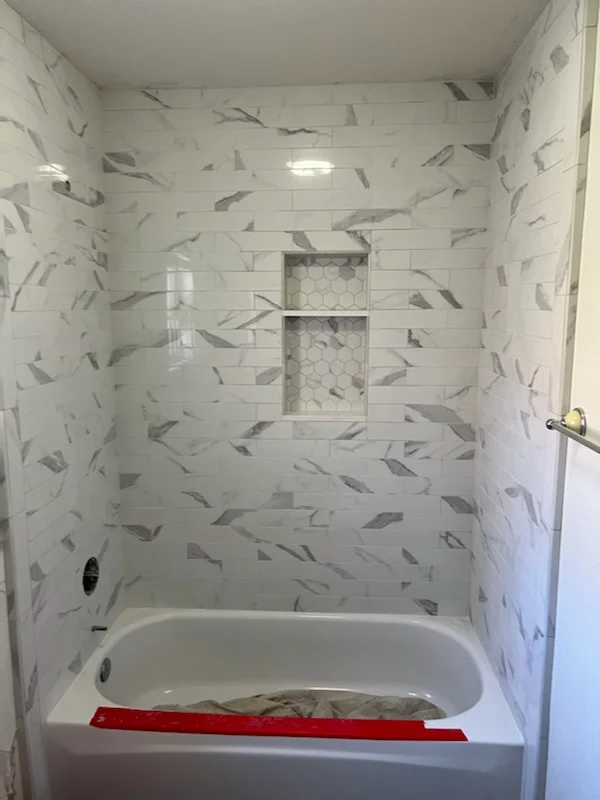 Marble-look subway tile shower surround with linear accent tiles and recessed niche