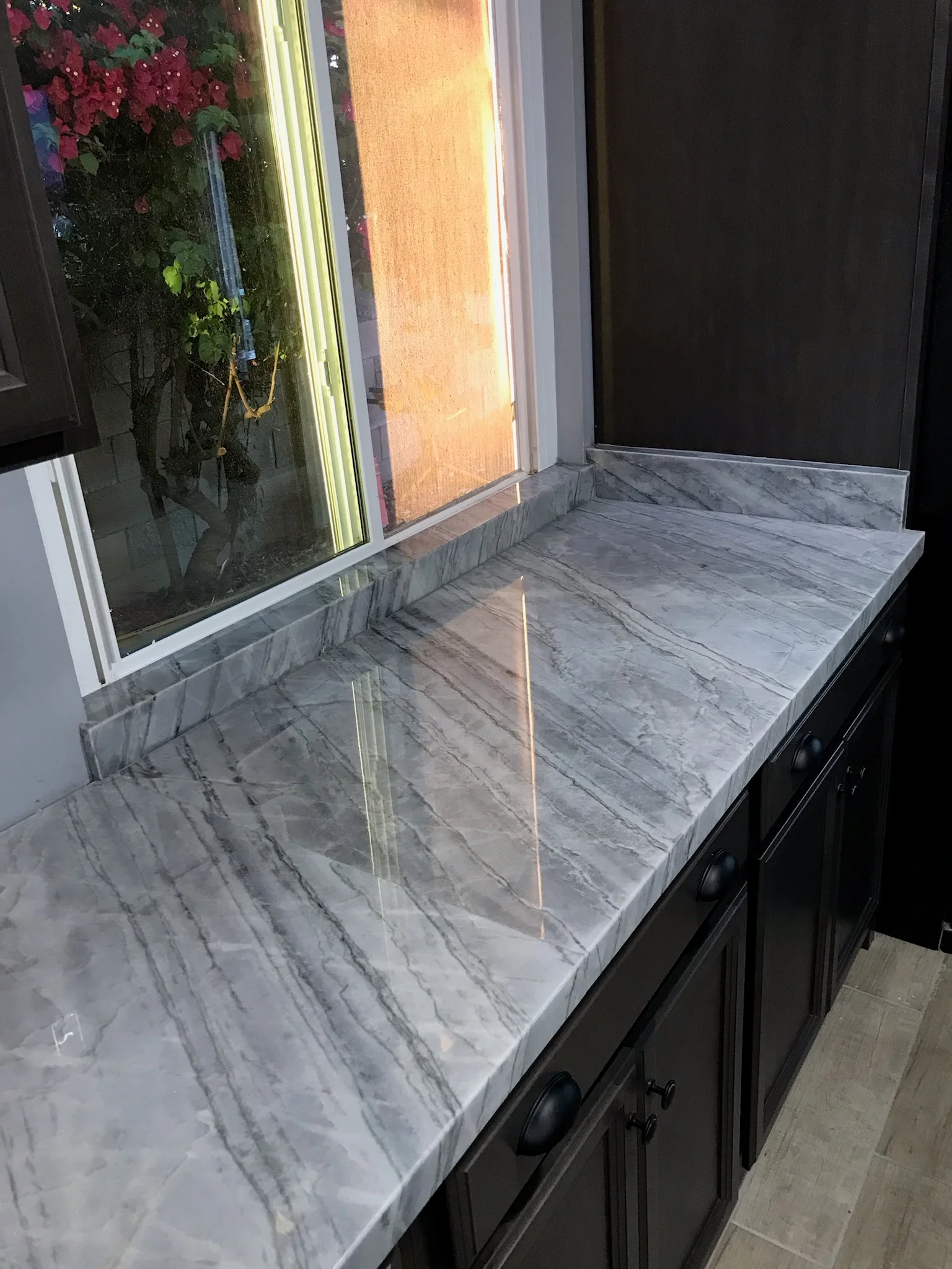 Gray marble countertop with white veining, polished finish, installed above black cabinetry with new window frame