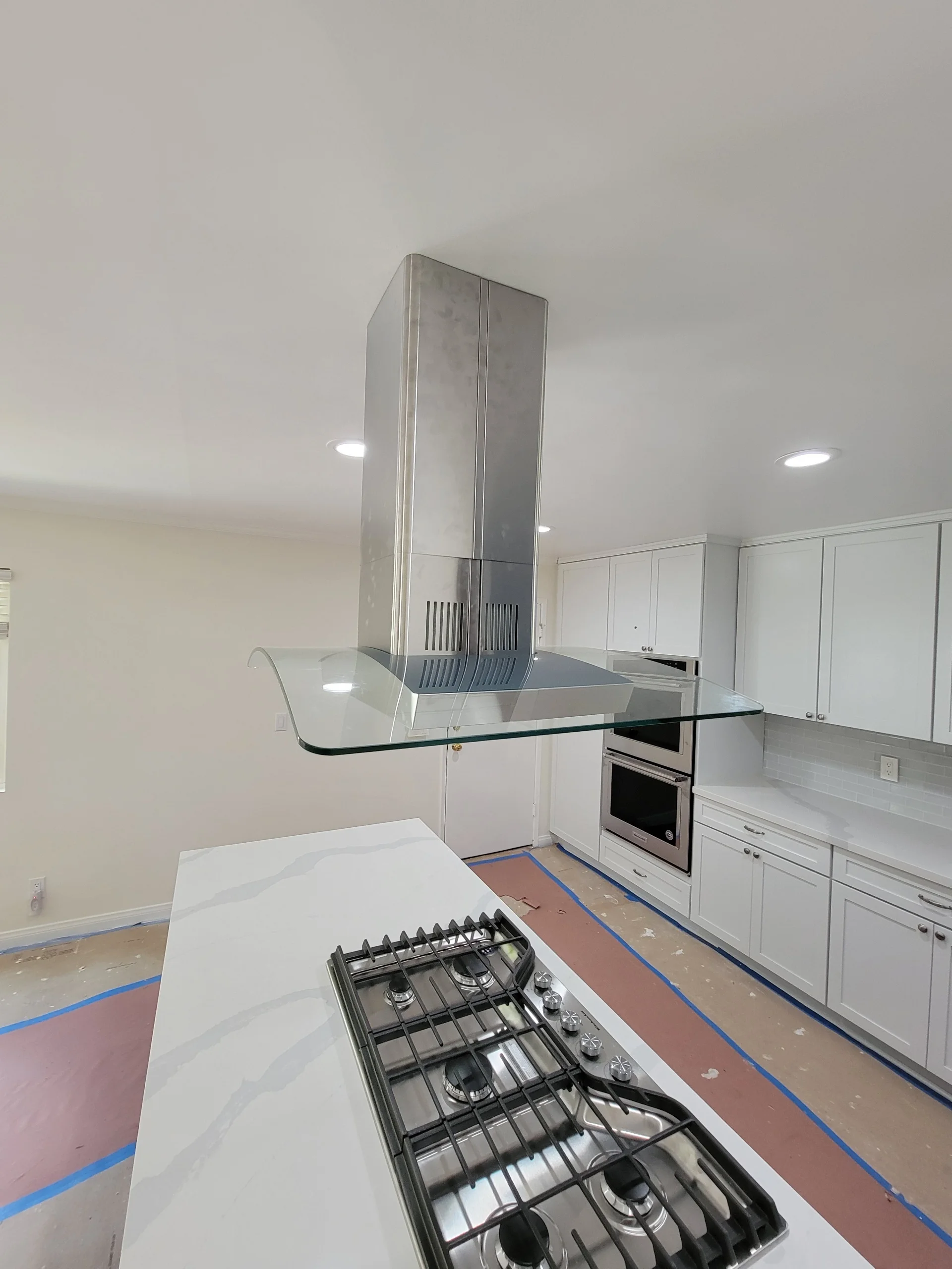 Kitchen renovation with white cabinets, gas range, stainless steel hood, and island countertop