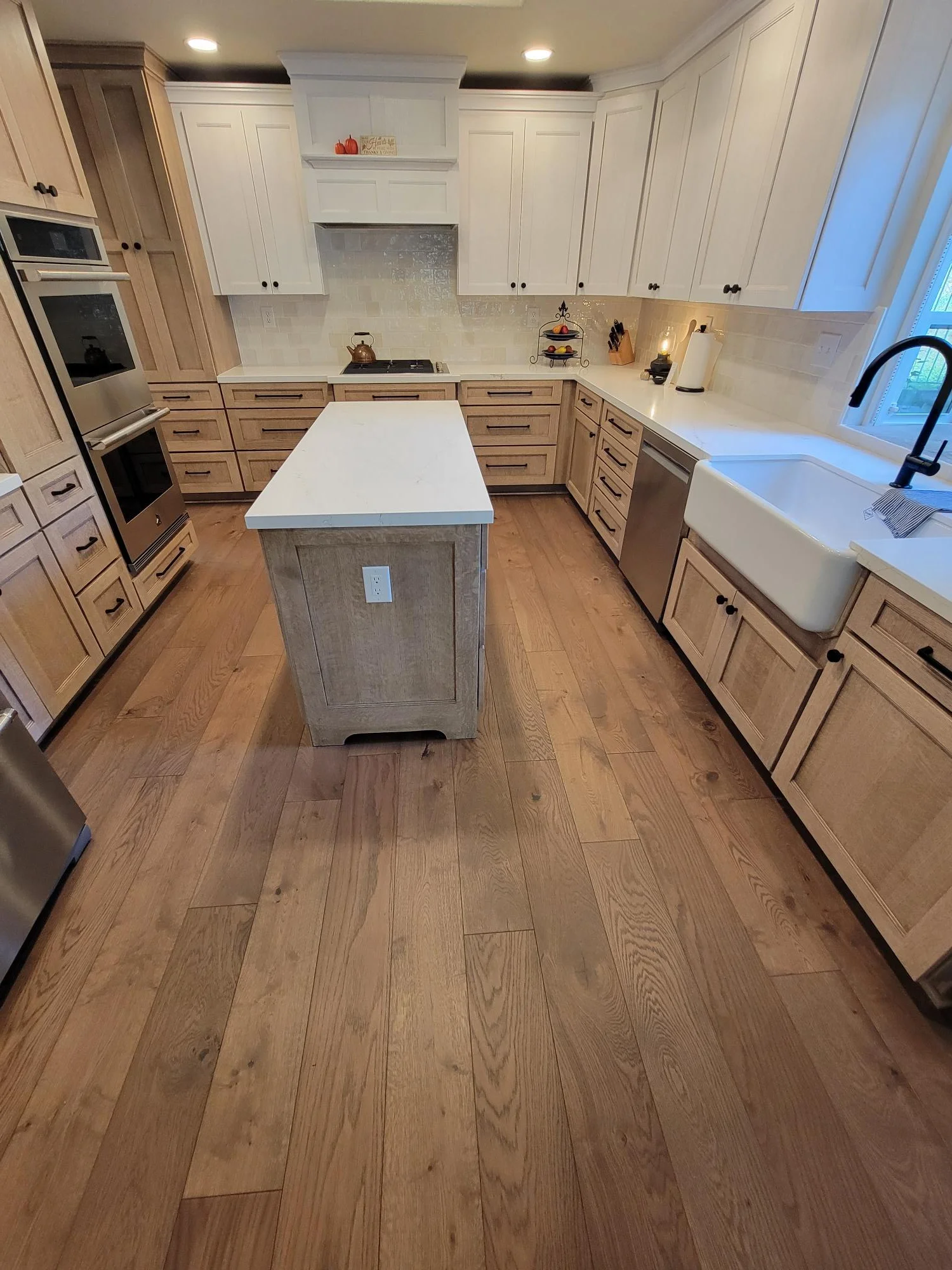 Kitchen remodel with white and wood cabinetry, quartz counters, island, hardwood floors, and stainless appliances