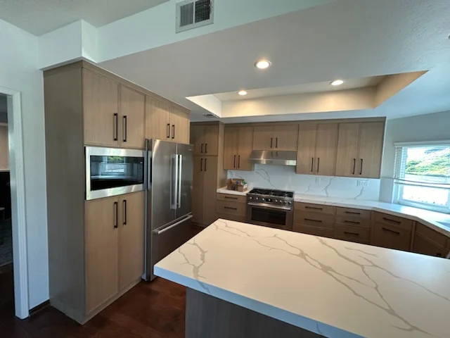 Modern kitchen with wood cabinetry, quartz countertops, stainless steel appliances, and recessed lighting