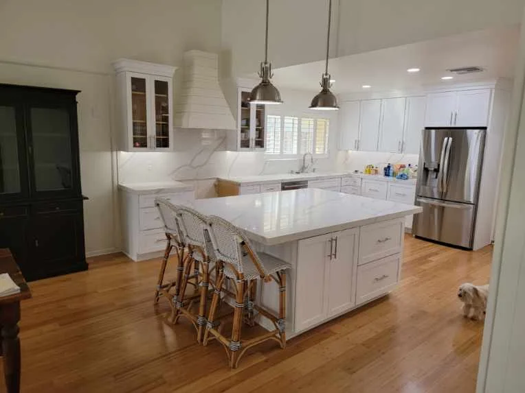 White kitchen with island, quartz counters, stainless steel appliances, hardwood floors, and pendant lighting