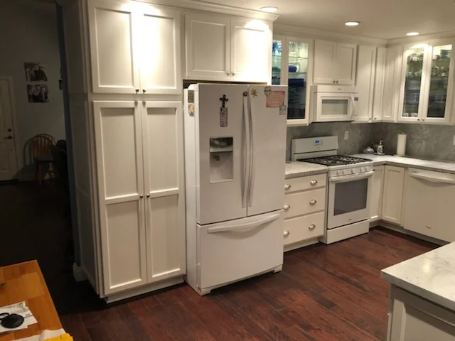 White kitchen with custom cabinetry, stainless steel appliances, and hardwood flooring