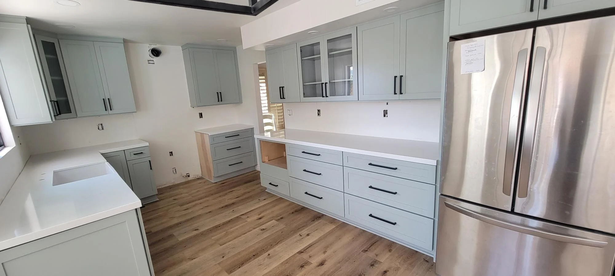 Light gray kitchen cabinets with black handles, white quartz counters, wood-look vinyl flooring, stainless steel appliances