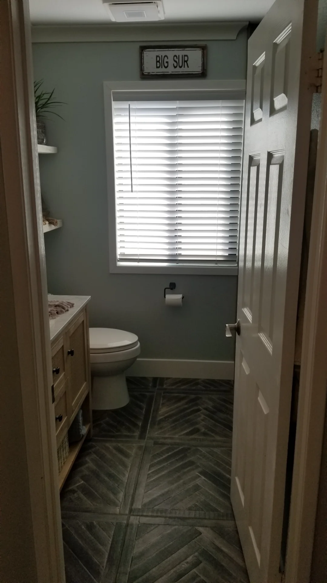 Bathroom with sage walls, white cabinetry, herringbone tile floor, and white shutters