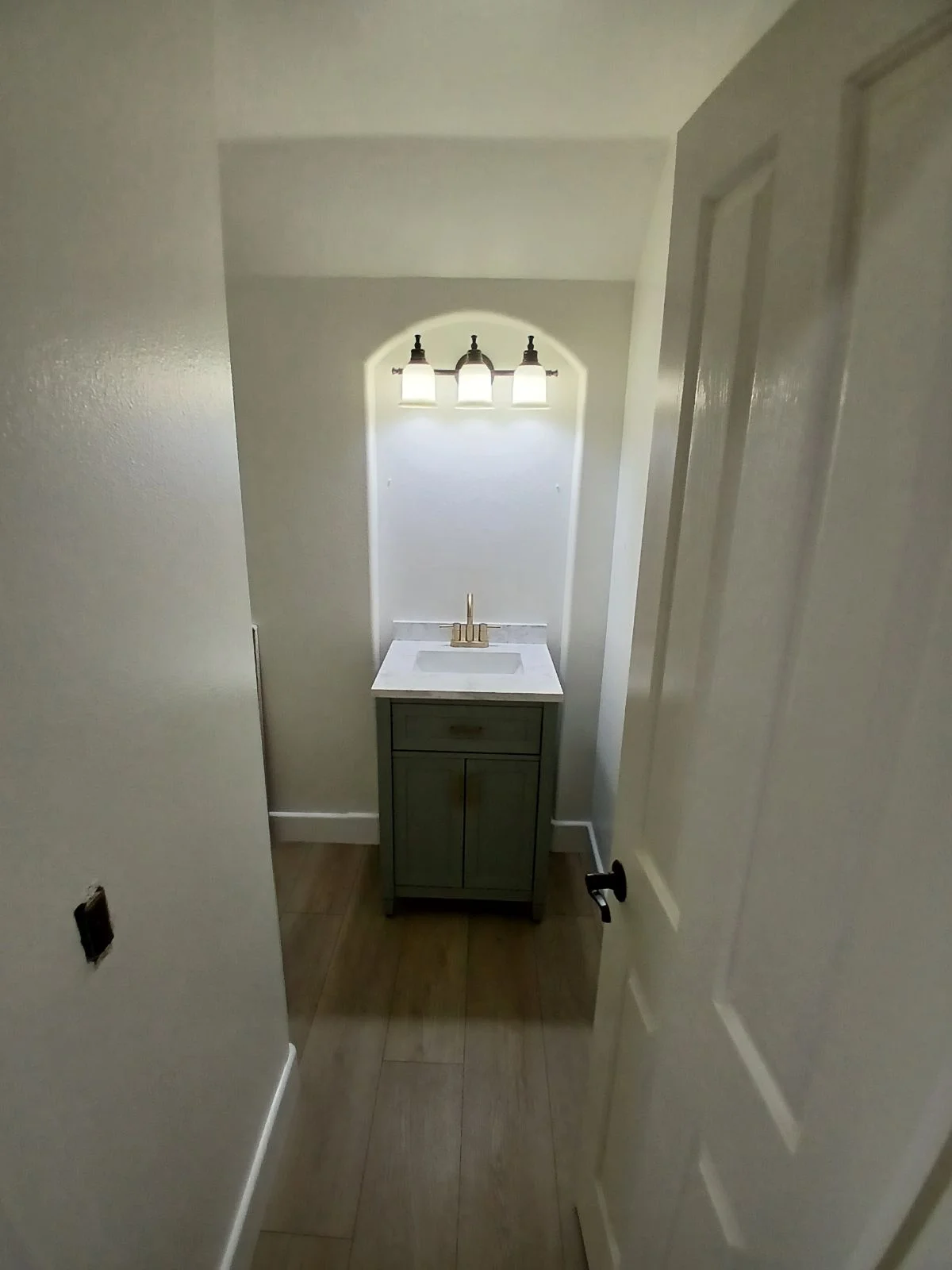 Bathroom vanity with dark cabinets, white quartz countertop, and three-light vanity fixture in arched alcove